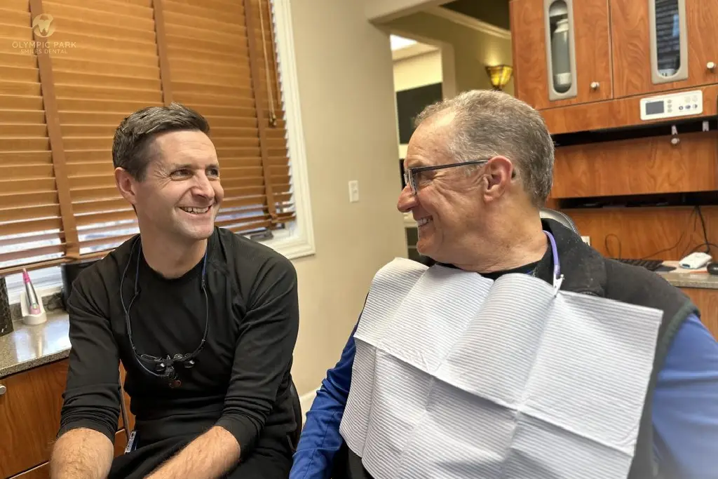 Smiling dentist talking with an older male patient wearing a dental bib