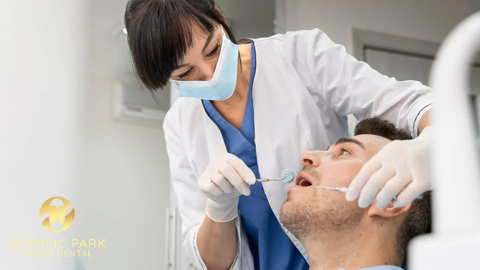Dentist in a face mask examining a male patient's teeth with a dental mirror